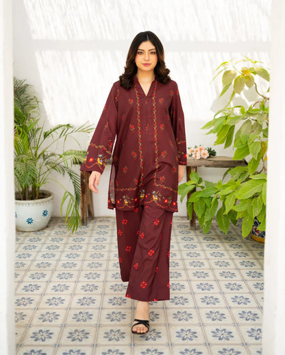 Woman in a maroon printed outfit standing in a room with plants and patterned tiles.