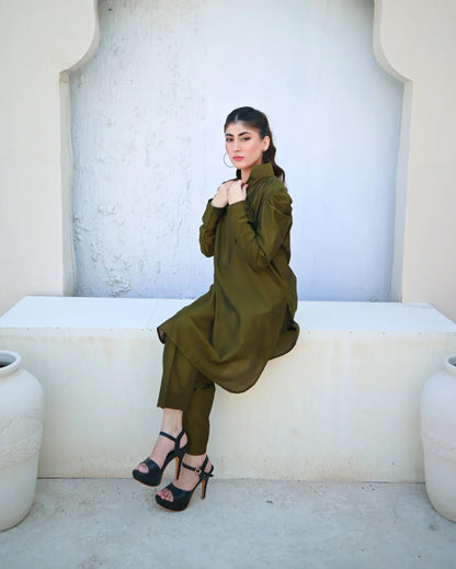 Woman in a green outfit sitting on a white bench with a textured wall background