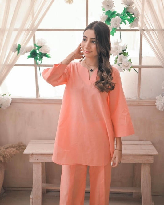 Woman wearing a peach-colored outfit standing in a decorated room with flowers and a wooden bench.