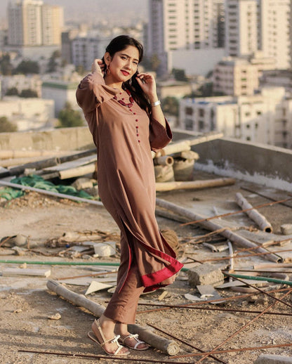 A woman in a brown dress with red accents standing on a rooftop.