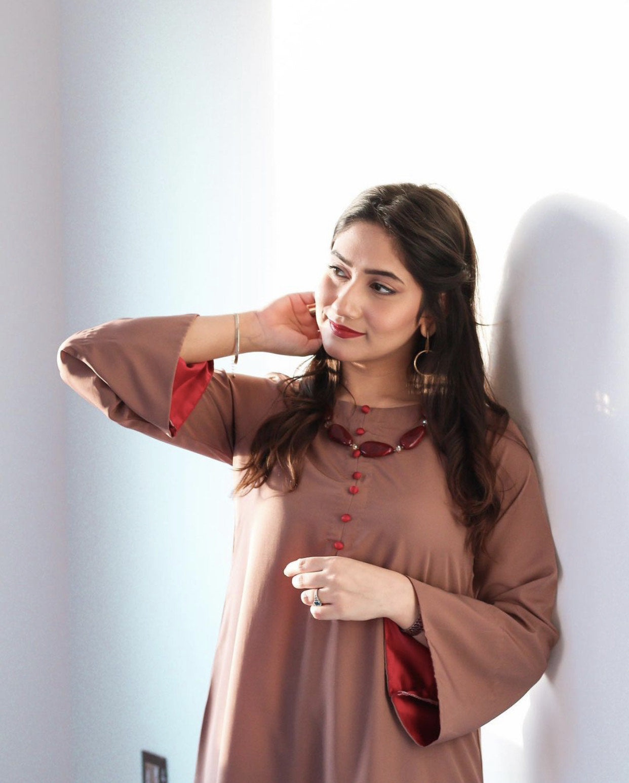A woman in a brown dress with red accents, exuding a relaxed and confident vibe, in a softly lit room.