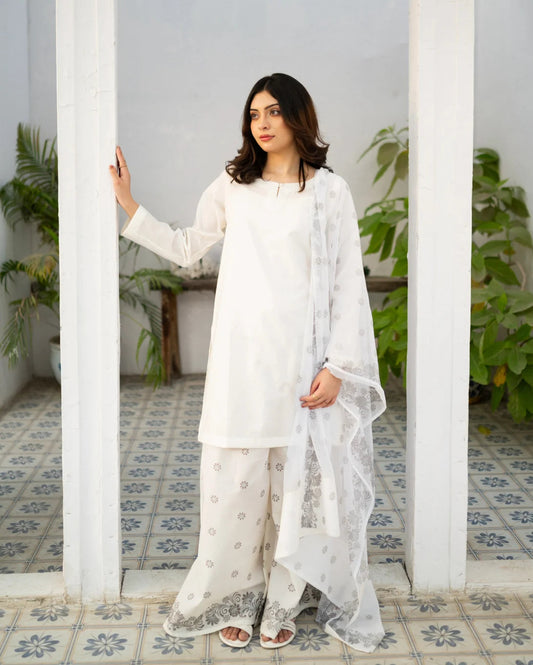 Woman in a white traditional kurta set standing in a room with white walls and tiled floor.